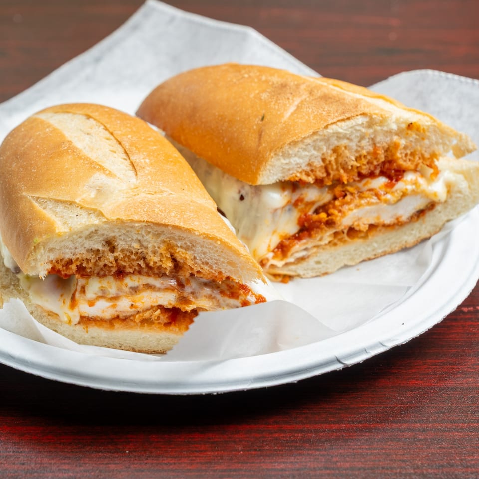 Two crusty baguette sandwiches filled with breaded chicken and red sauce on a paper-lined plate.