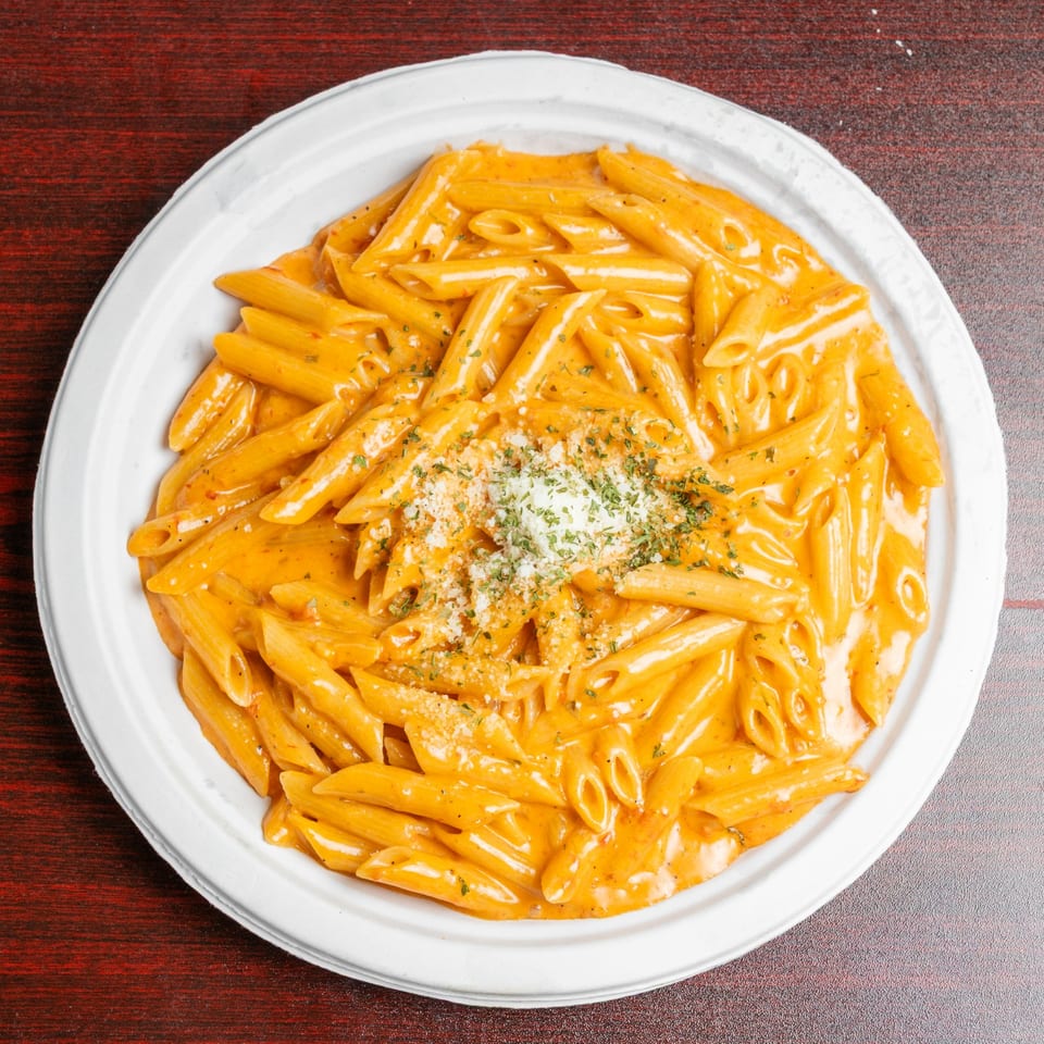 Penne pasta coated in creamy orange sauce, topped with grated cheese and herbs, served on a white plate.