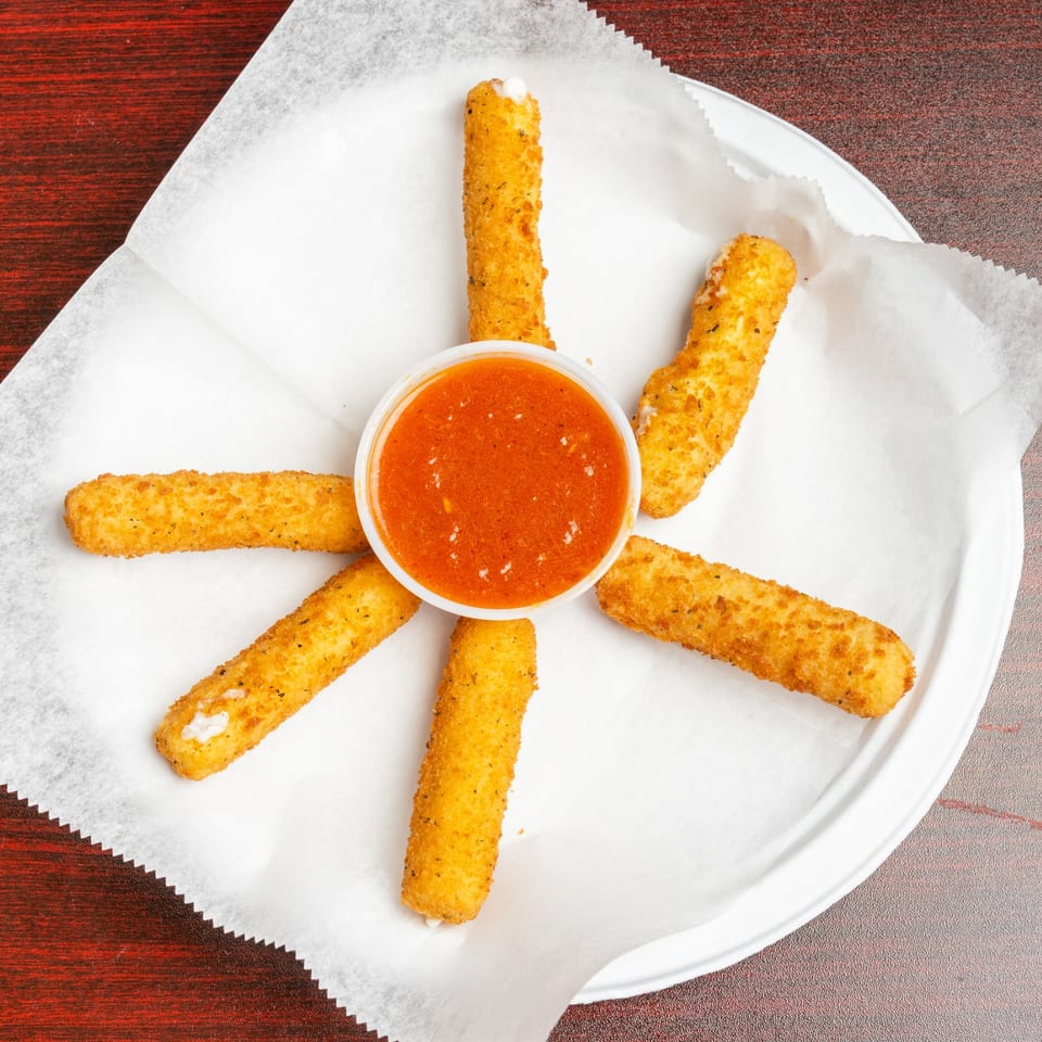 Six golden-breaded mozzarella sticks arranged around a cup of marinara sauce on a paper-lined plate.