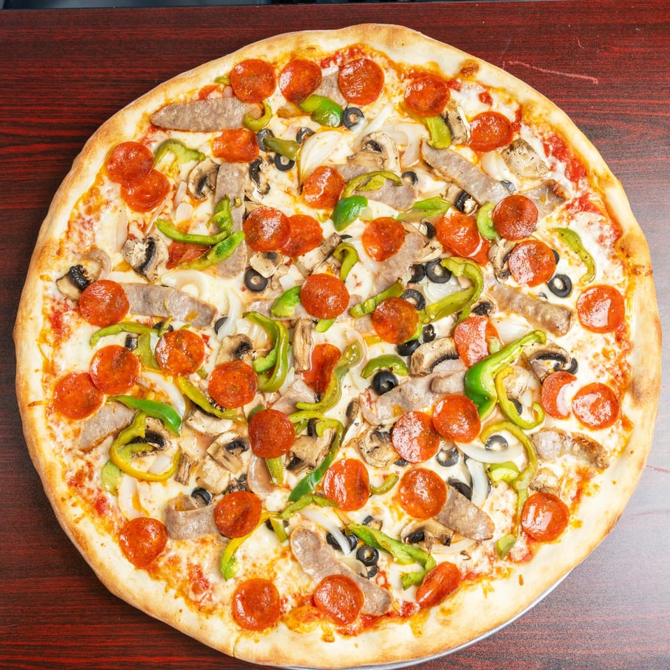 Loaded pizza topped with pepperoni, sausage, mushrooms, green peppers, onions, black olives, cheese, and tomato sauce on a wooden table.