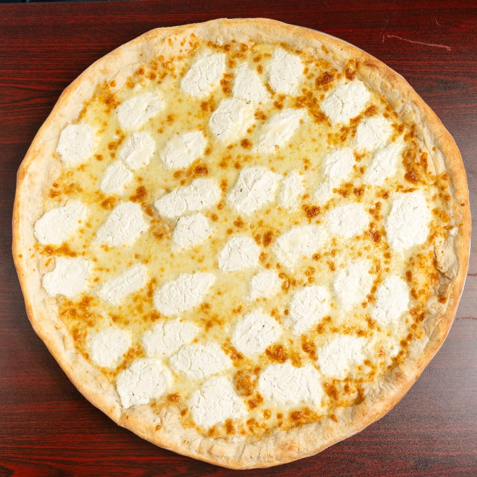Round white cheese pizza with golden-browned crust and scattered melted cheese pieces on a dark wooden table.