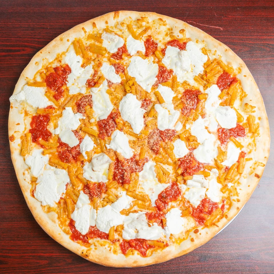 Round pizza topped with tomato sauce, mozzarella cheese, and penne pasta on a dark wooden table.