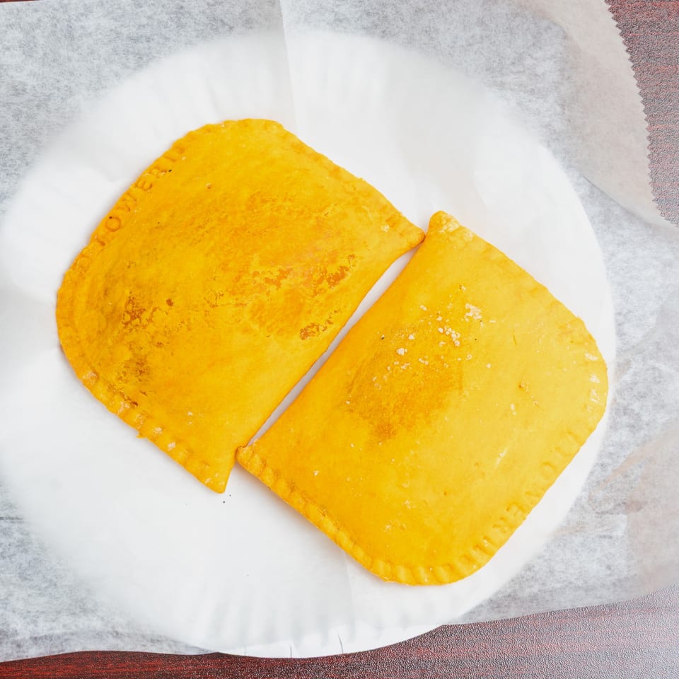 Two golden-brown, square fried pastries with crimped edges rest on white parchment paper.