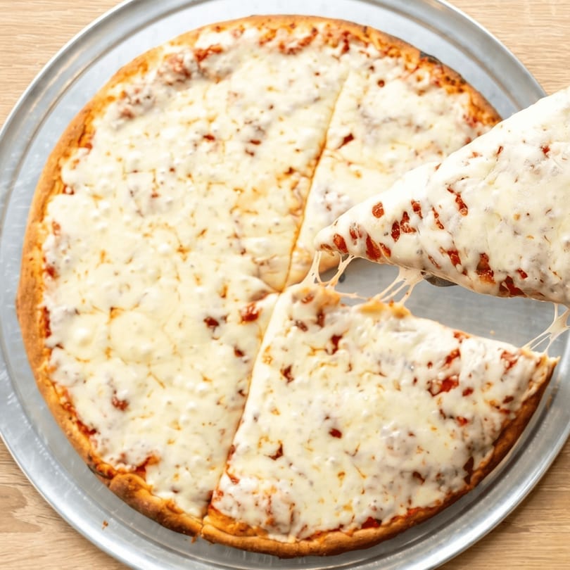 A cheesy pizza on a metal tray with one slice being lifted, showing melted cheese stretching.
