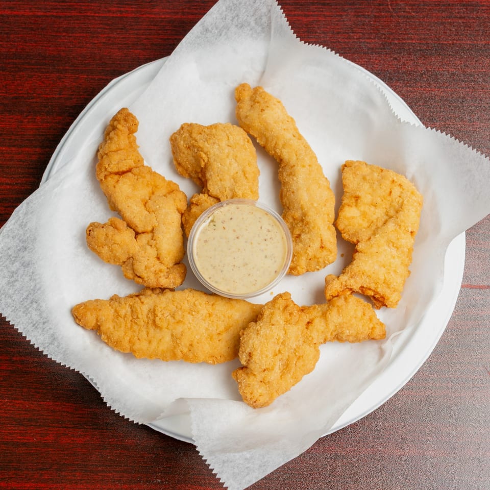 Golden fried chicken tenders arranged around a cup of creamy dipping sauce on a paper-lined plate.