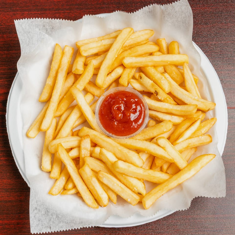 Golden French fries served on parchment paper with a cup of ketchup on a white plate.